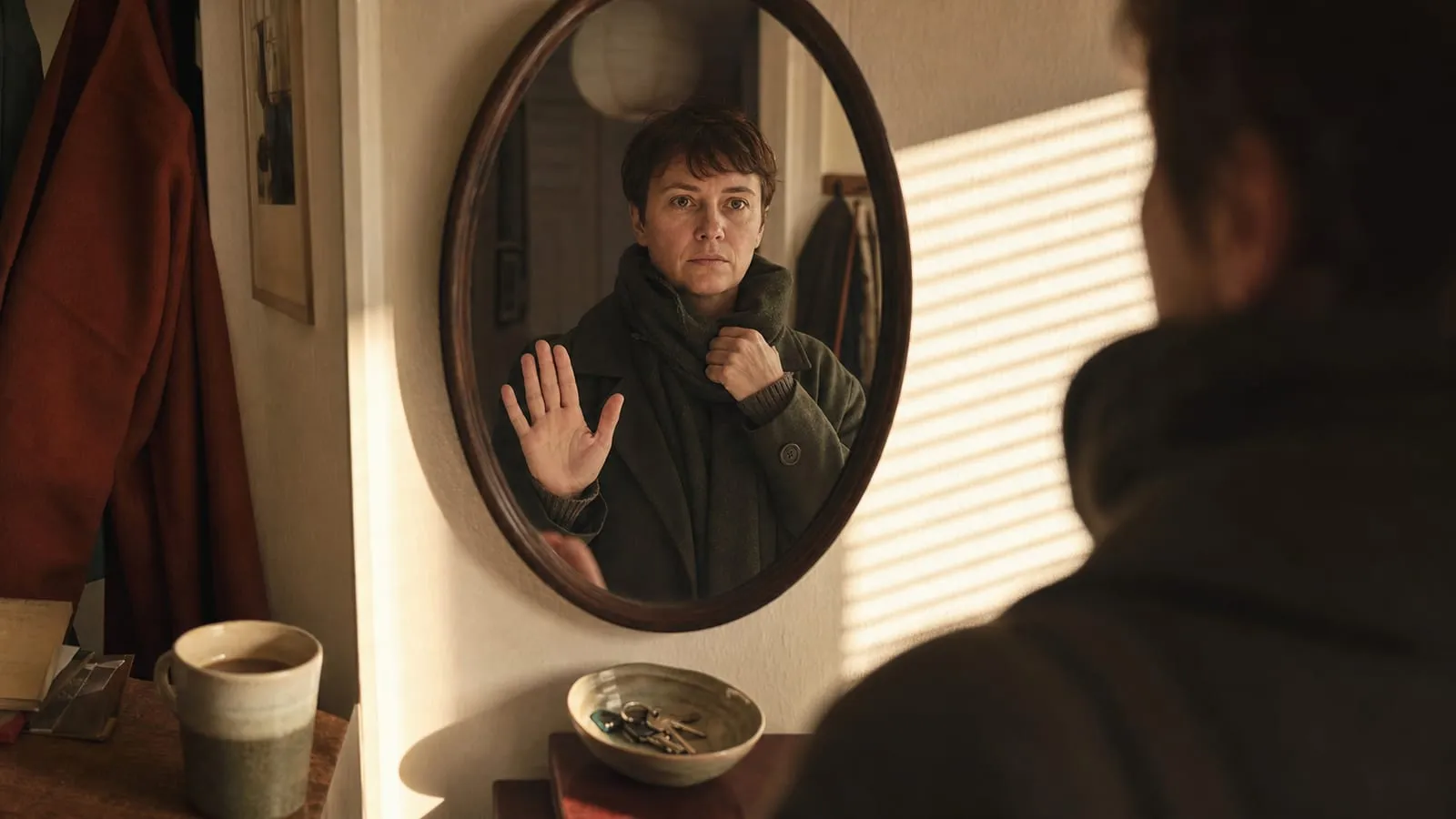 Choosing a dentist when anxious: a person rehearses a raised-hand stop signal in a softly lit hallway mirror before leaving home.