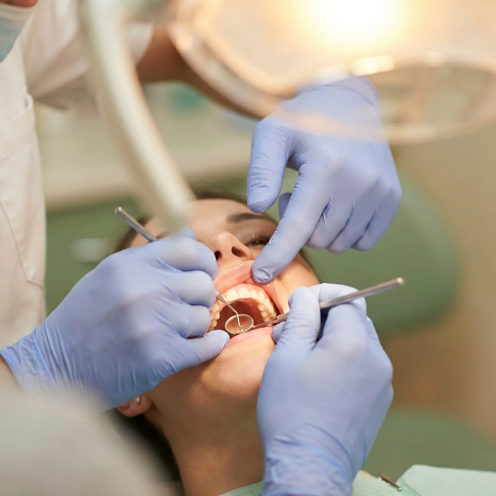 Gloved hands examine a patient's teeth with a mirror and probe.