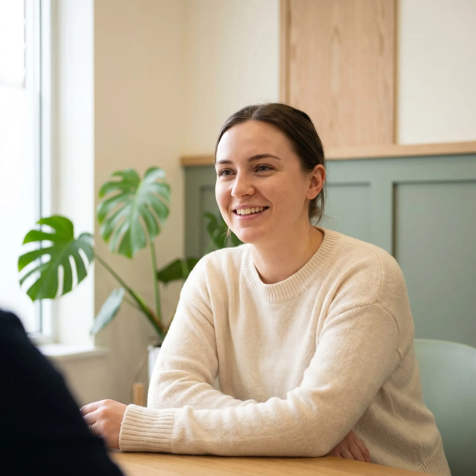 A smiling woman talks across a table in a bright consultation room.